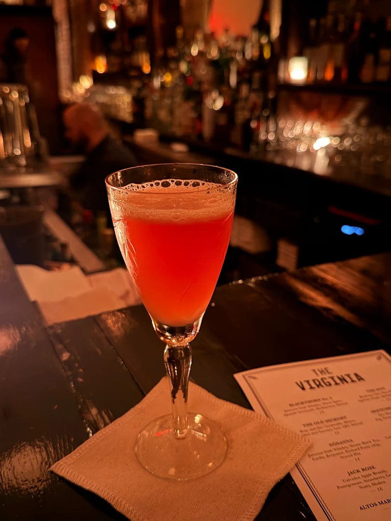 Coral-pink shaken cocktail in a stemmed glass beside The Virginia menu