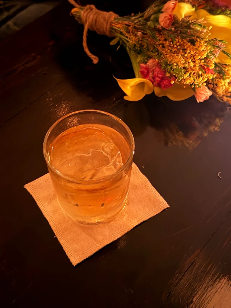 Whiskey on a coaster beside a small bouquet on the bar
